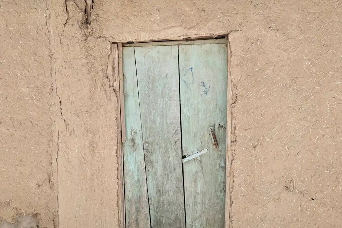A weathered wooden door set into an earthen wall with visible cracks around the frame.