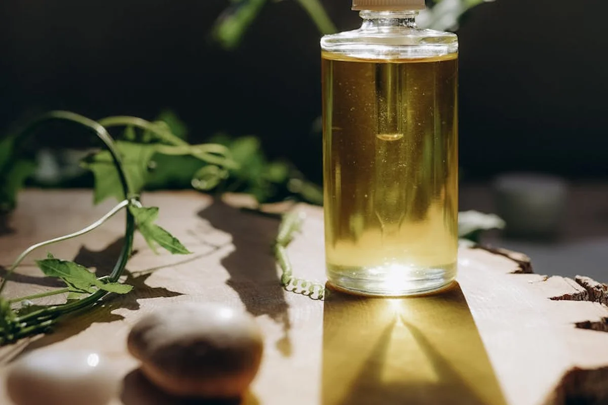 Glass bottle of pale oil on a wooden tabletop with green leaves in the background, illustrating natural oil finishes.