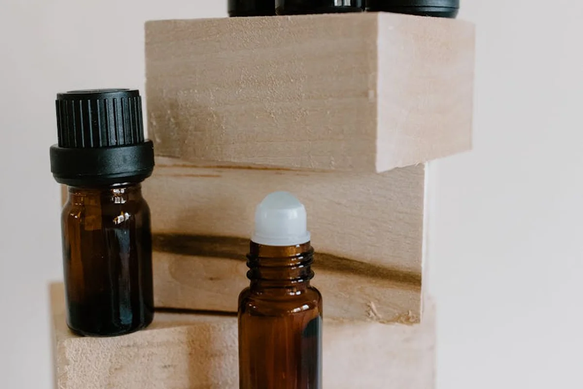 Amber glass bottles containing wood oil finishes sit on light wooden blocks; one bottle has a dropper cap and another has a screw-top lid.