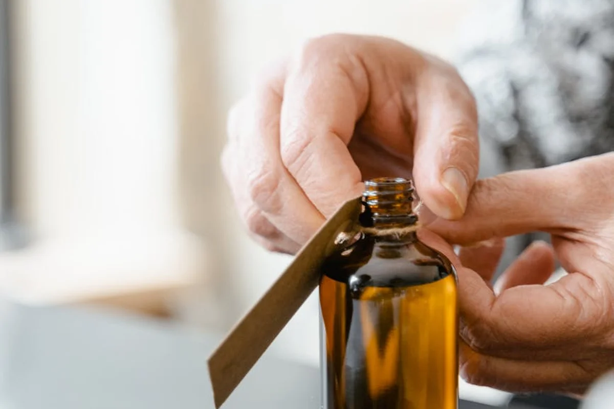 Close-up of hands handling an amber glass bottle of finishing oil with a metal spatula resting nearby