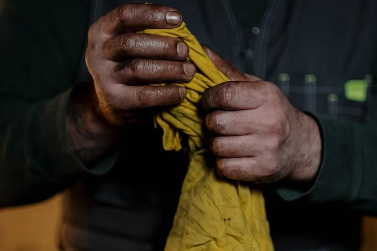 Close-up of hands wringing a yellow cloth rag, stained with oil.