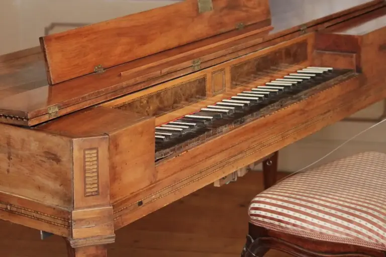 An antique upright piano with a worn, patinated wooden finish and a striped upholstered chair nearby.