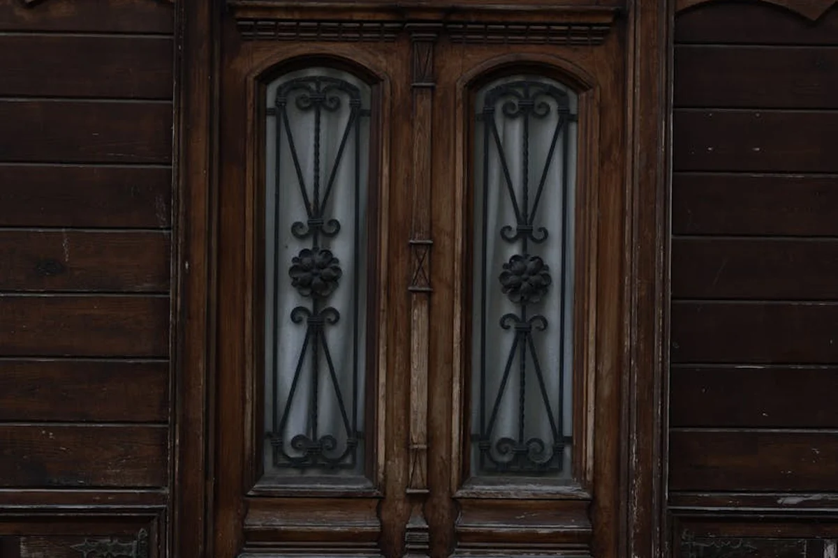 Pair of dark wooden doors with ornate wrought-iron panels and central handles.