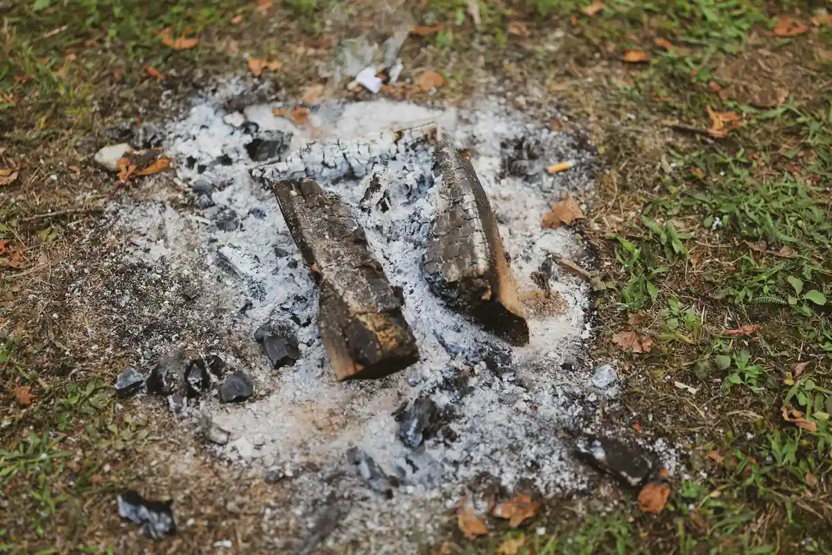 Pile of wood stove ashes and charred debris on the ground outdoors.