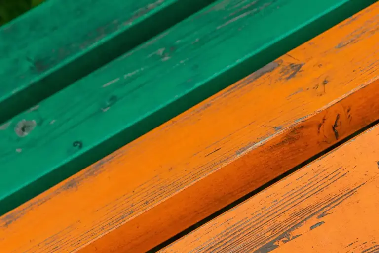 Close-up of weathered outdoor wood planks painted green and orange, showing wear and moisture exposure.