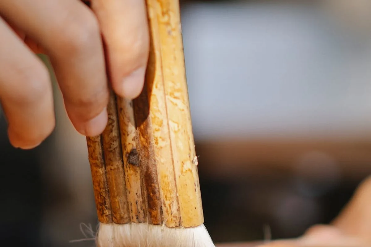 Close-up of a hand applying wood glue to wooden slats for outdoor furniture using a brush.