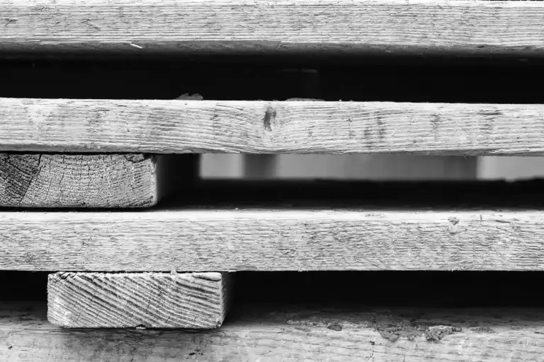 Grayscale image of stacked wooden pallets with weathered boards and gaps