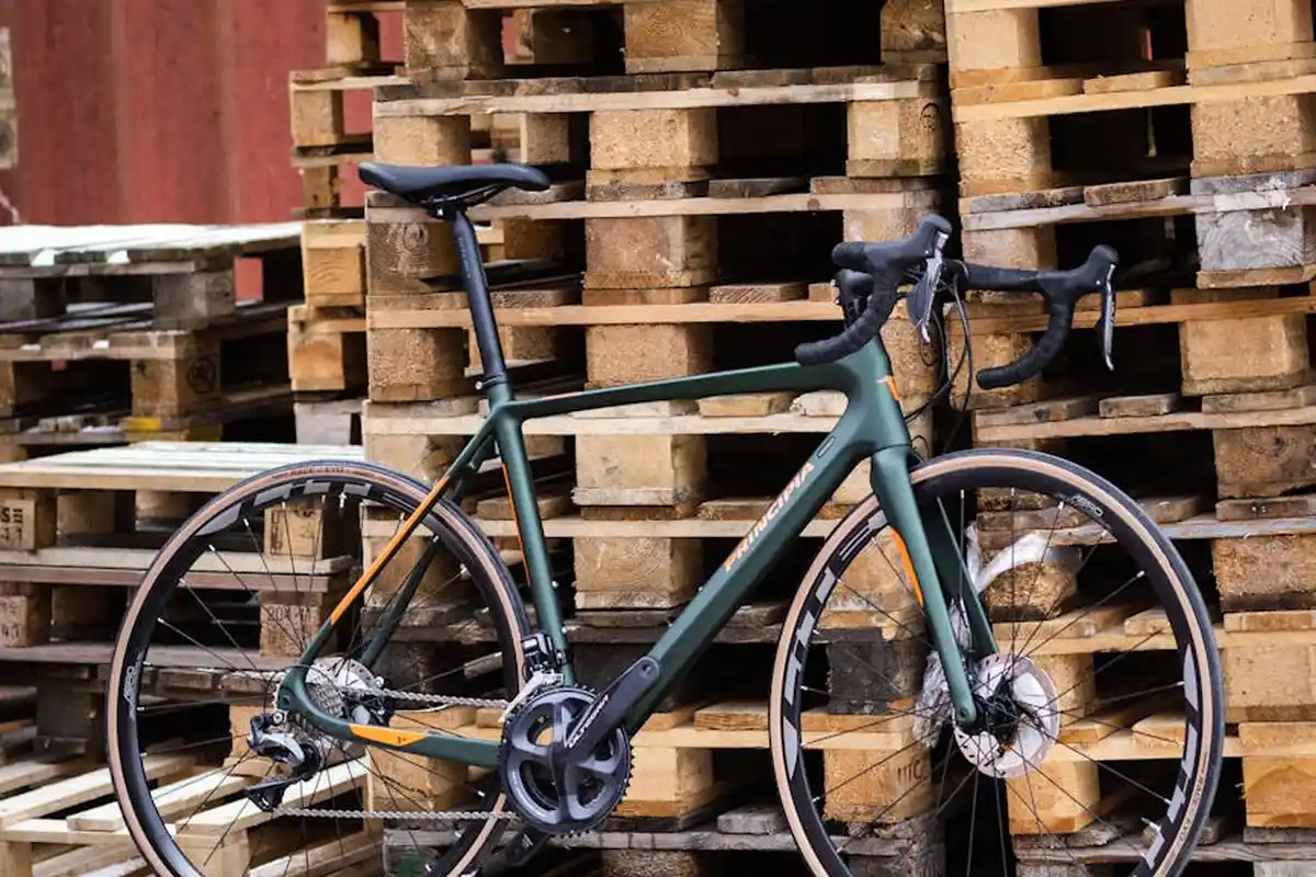 A green bicycle leaning against stacked wooden pallets in a yard, with weathered boards and pallets towering behind.