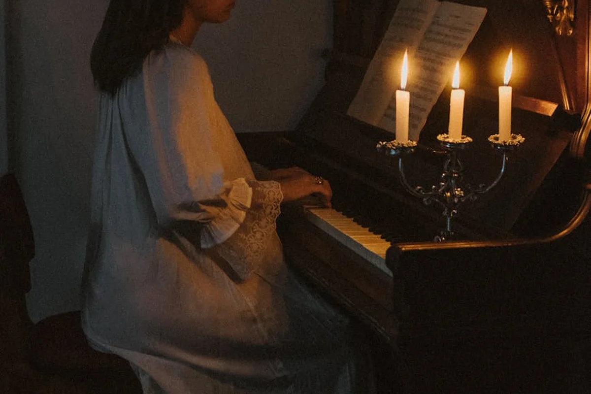 Person playing a piano in a dimly lit room with candles on a music stand and sheet music