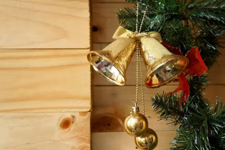 Close-up of pine wood planks with golden Christmas bells and evergreen branches in the background.