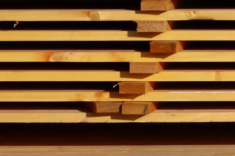 Stack of orange-brown pressure-treated lumber planks laid in horizontal layers, ready for outdoor projects.
