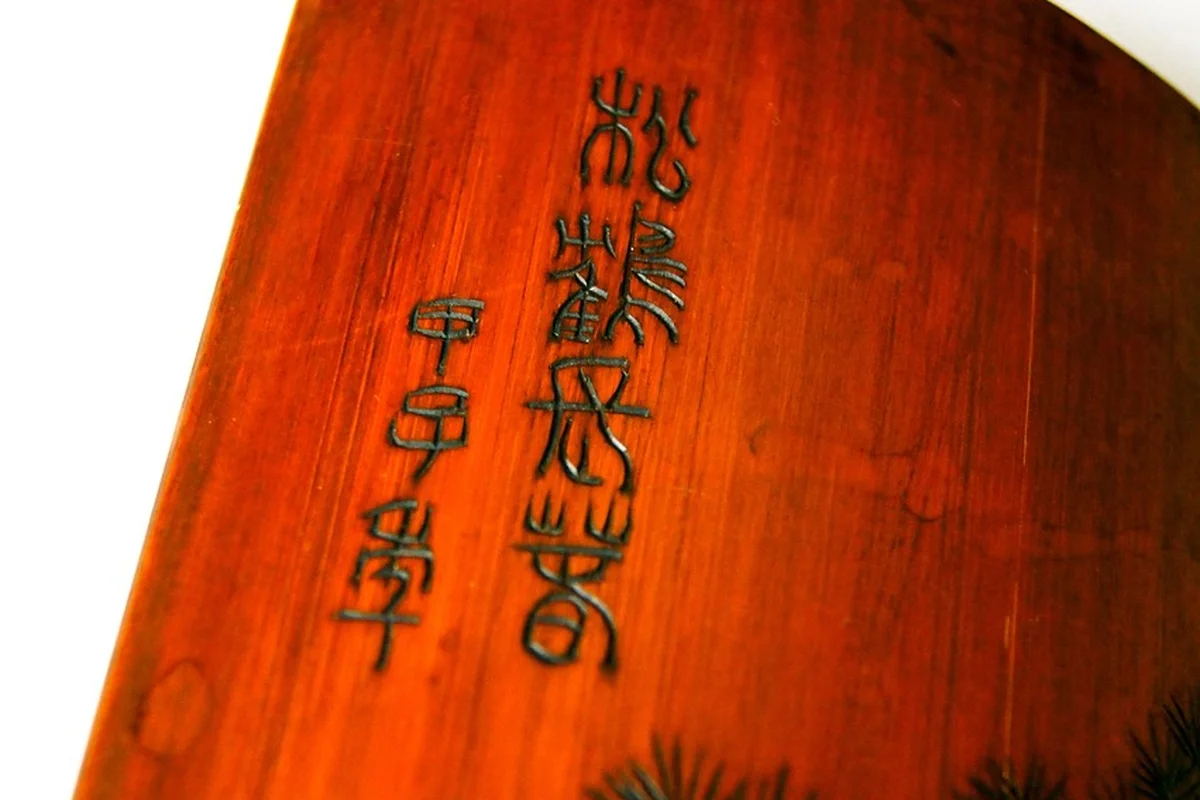 Close-up of a red-brown pressure-treated wooden plank with vertical carved inscriptions