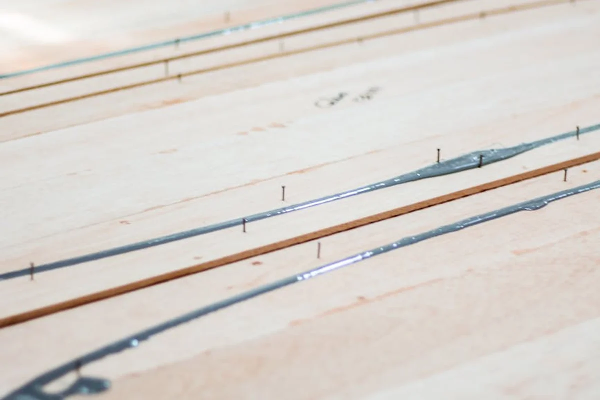Close-up of wooden boards with adhesive lines applied along joints and visible nails, illustrating prepared surfaces for gluing.