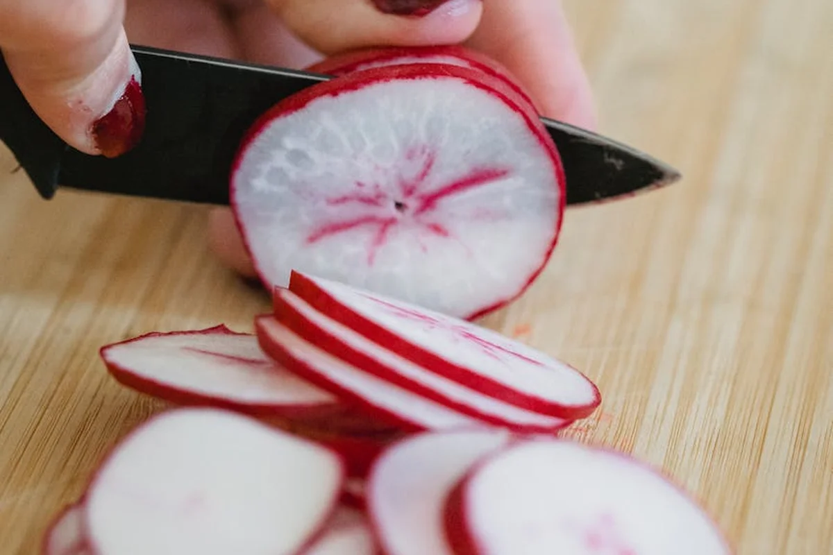 Close-up of thinly sliced radishes on a wooden cutting board with a knife nearby.