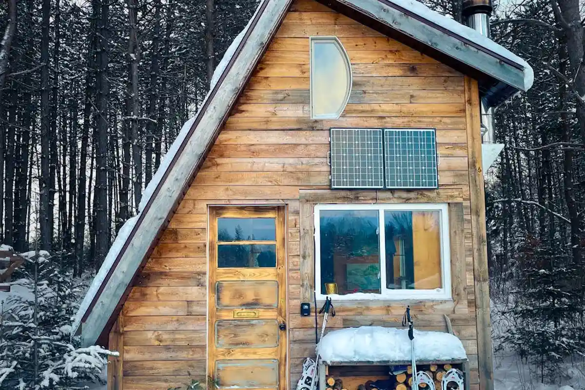 Snow-covered wooden pine cabin with solar panels in a forest