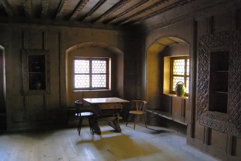 Dim historic room with carved wooden paneling, a small table, and wooden chairs, illustrating antique furniture that benefits from gentle cleaning to preserve its patina.