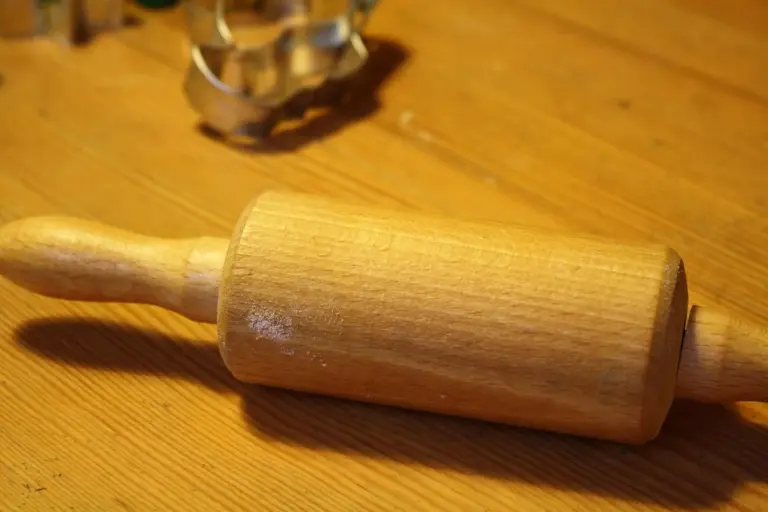 A wooden rolling pin resting on a warm wooden kitchen counter, showing the wood grain.