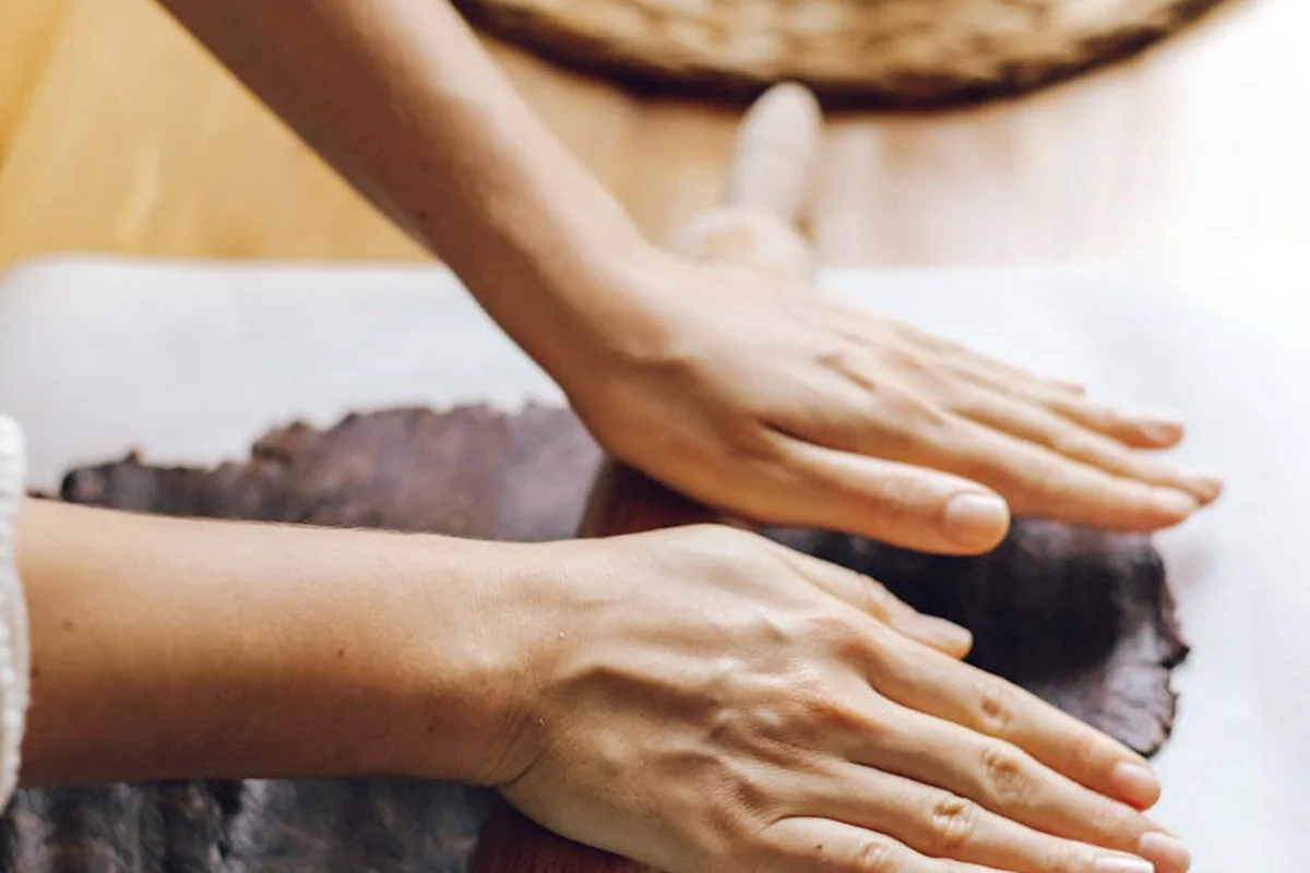 Close-up of hands rolling dough on a wooden work surface with a rolling pin blurred in the background.