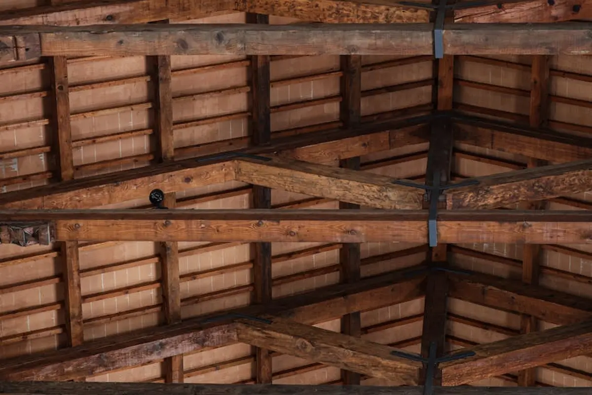 Interior view of a timber-framed roof with exposed beams and planks.