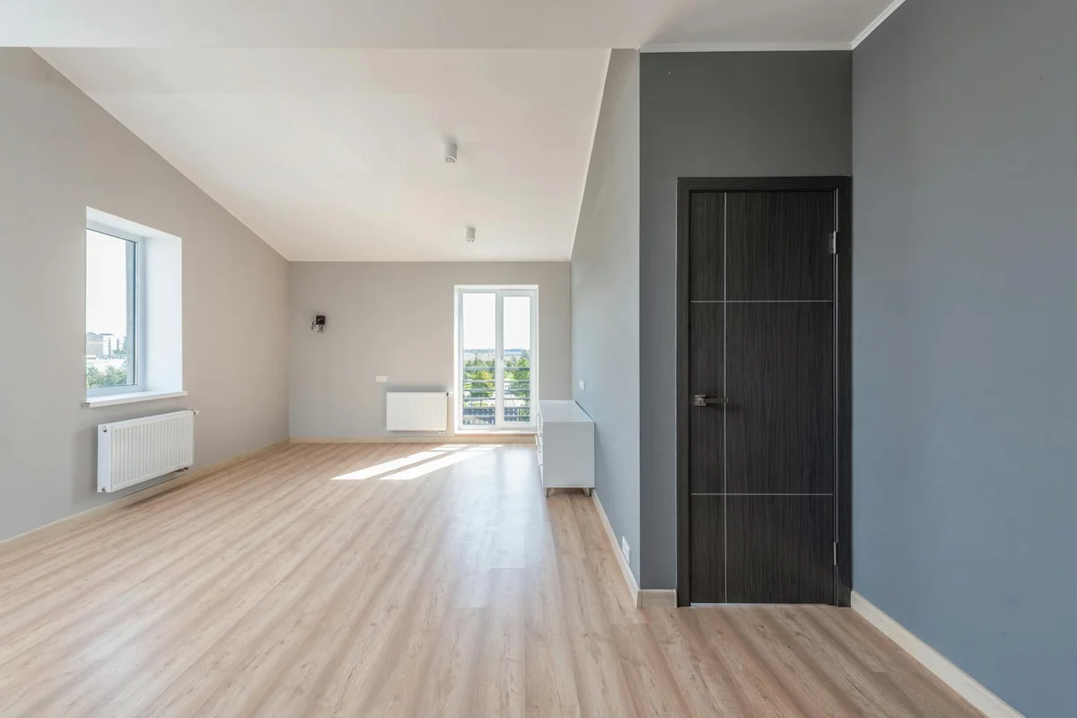Interior room with light hardwood flooring, gray walls, a dark door, and windows