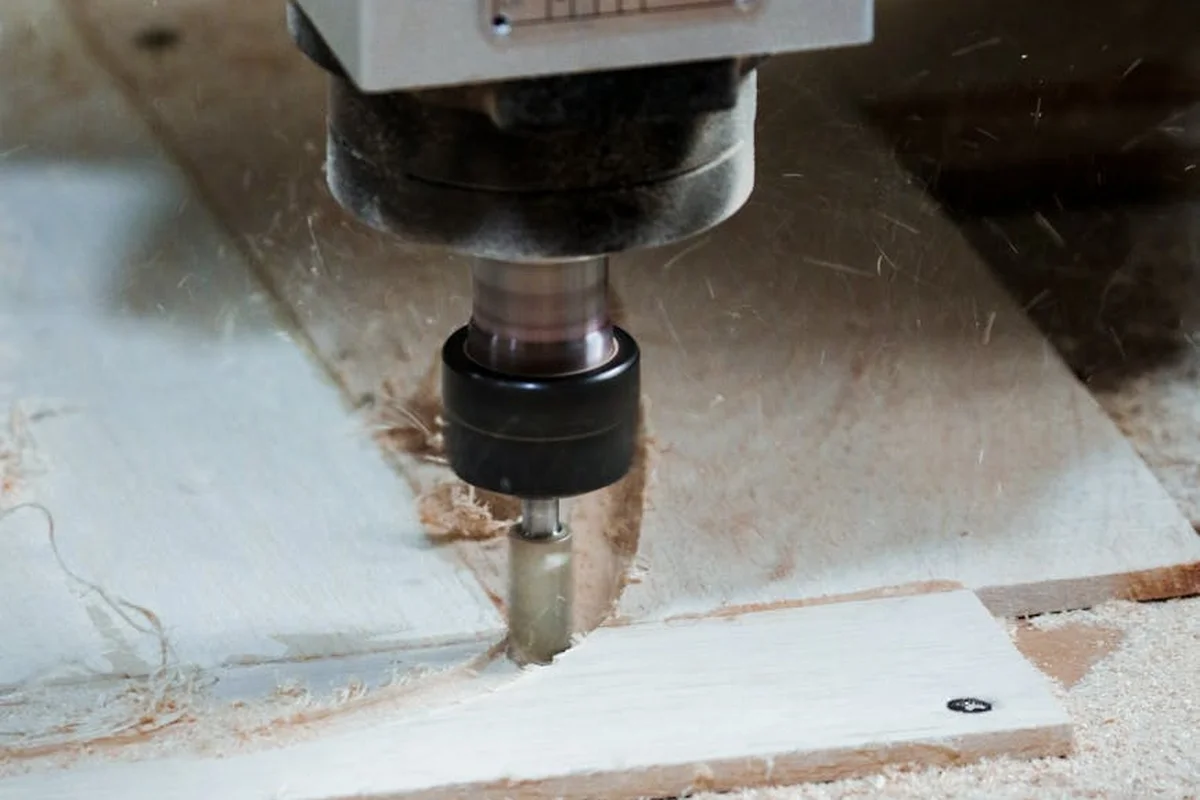 Close-up of a router bit cutting a wooden board, releasing wood dust in a workshop