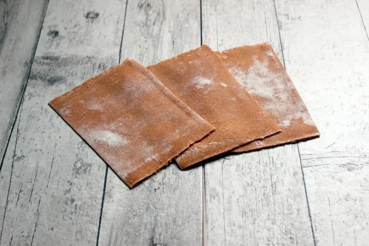 Three brown sheets of sandpaper placed on a light wooden surface, ready for surface preparation.