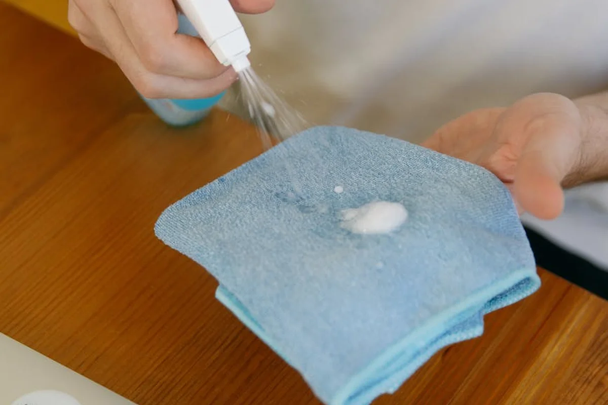 A blue microfiber cloth laid on a wooden surface as a dropper adds liquid to the fabric, preparing a basic scratch-test.