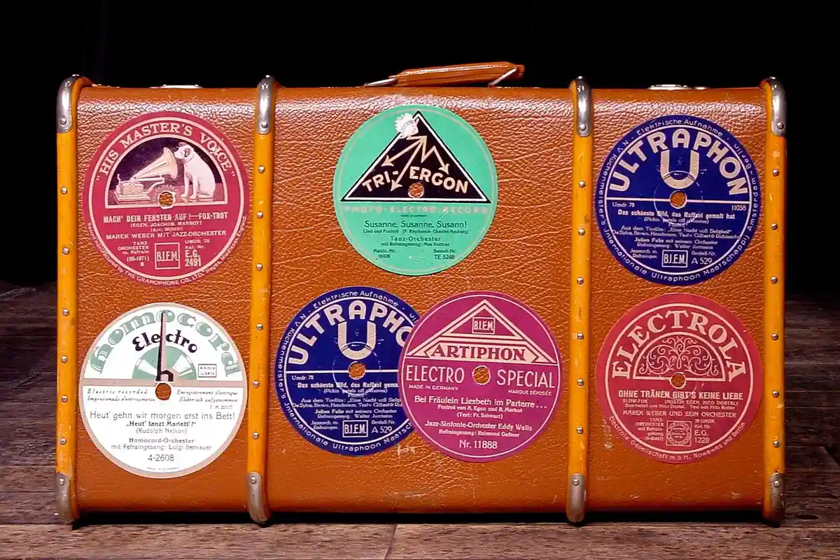 A vintage brown suitcase covered with colorful circular shellac label stickers, representing historical labeling and testing contexts for shellac finishes.