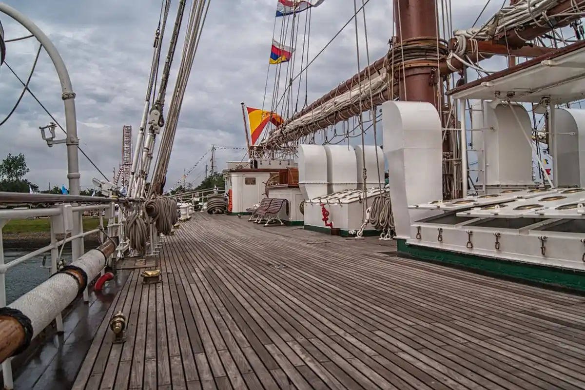 Wooden deck of a sailing ship with rigging and masts, showing weathered planks.