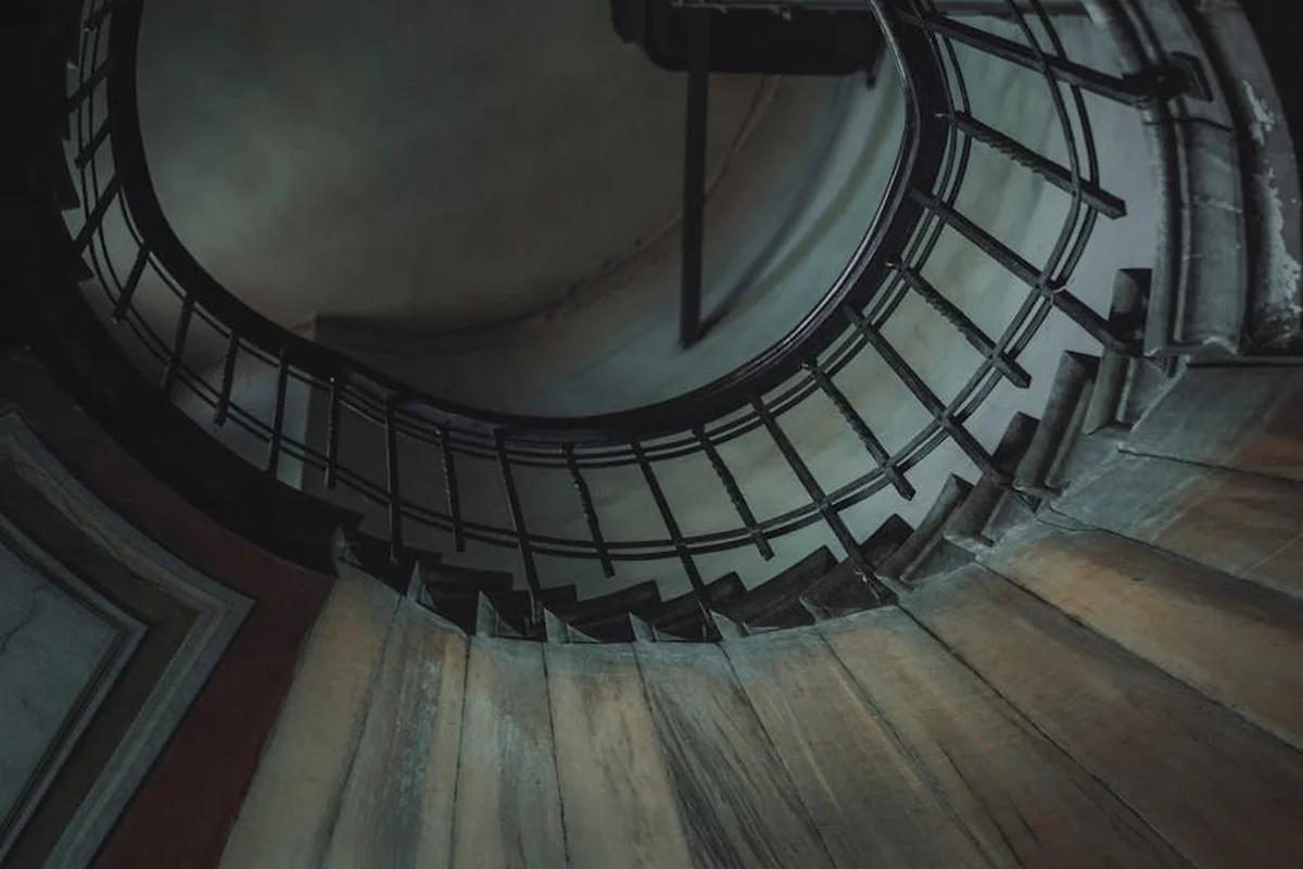 Interior spiral wooden staircase with curved treads and a metal railing, viewed from the center.