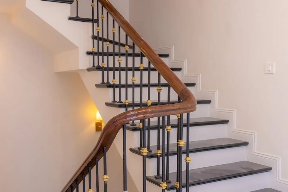 Wood staircase with a curved wooden handrail and black metal balusters with gold caps