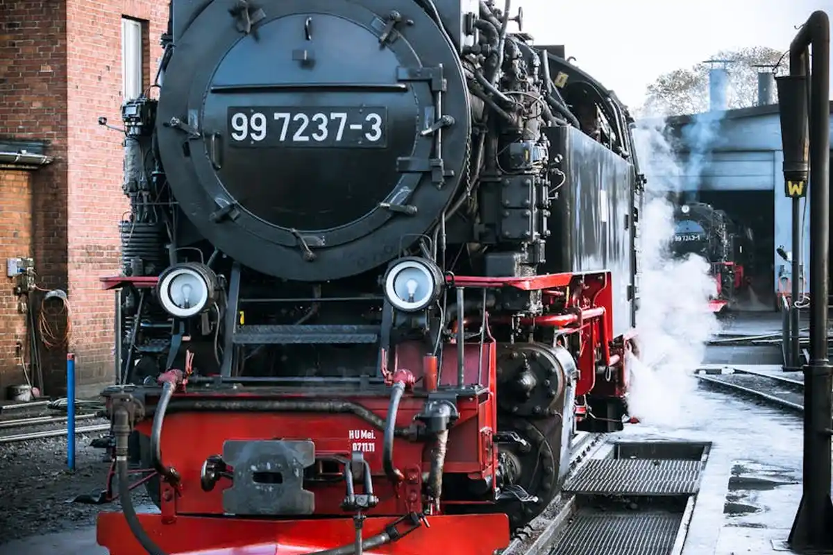 Front view of a black steam locomotive with a red undercarriage, bearing the number 99 7237-3, at a rail yard.