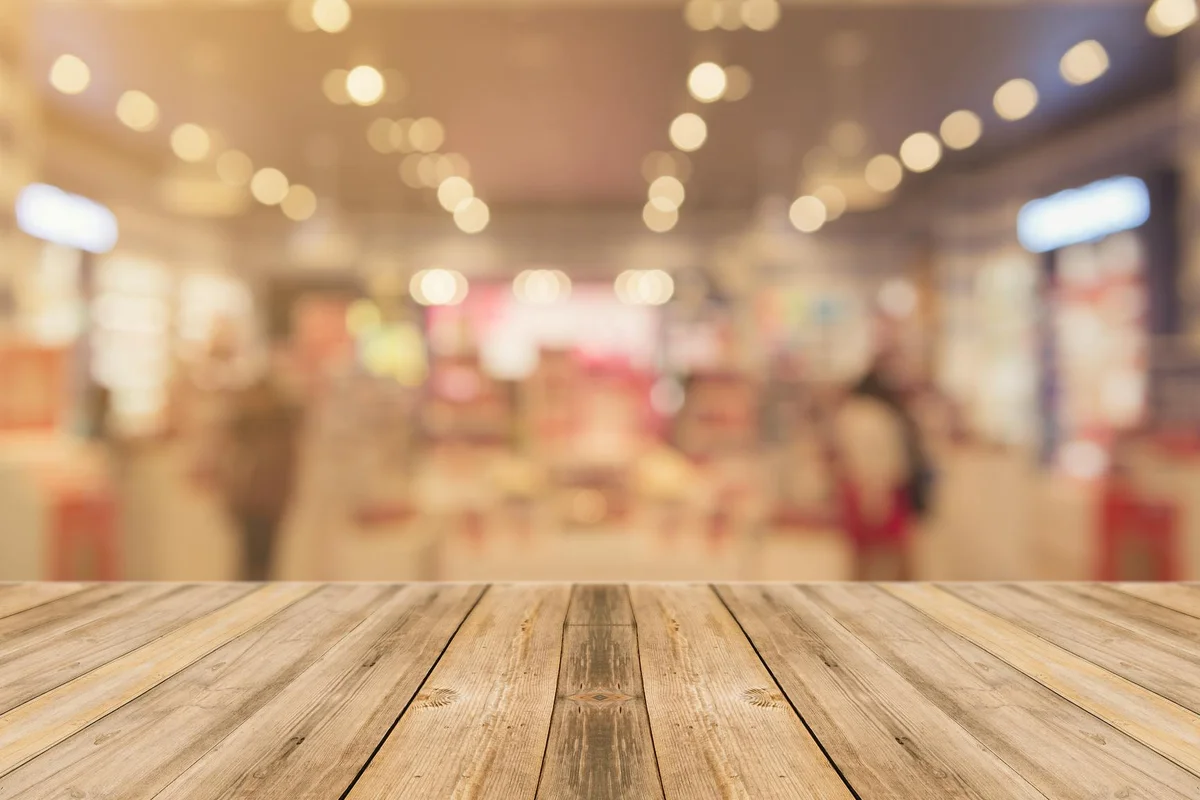 Foreground wooden tabletop with a blurred showroom or woodworking store interior in the background.