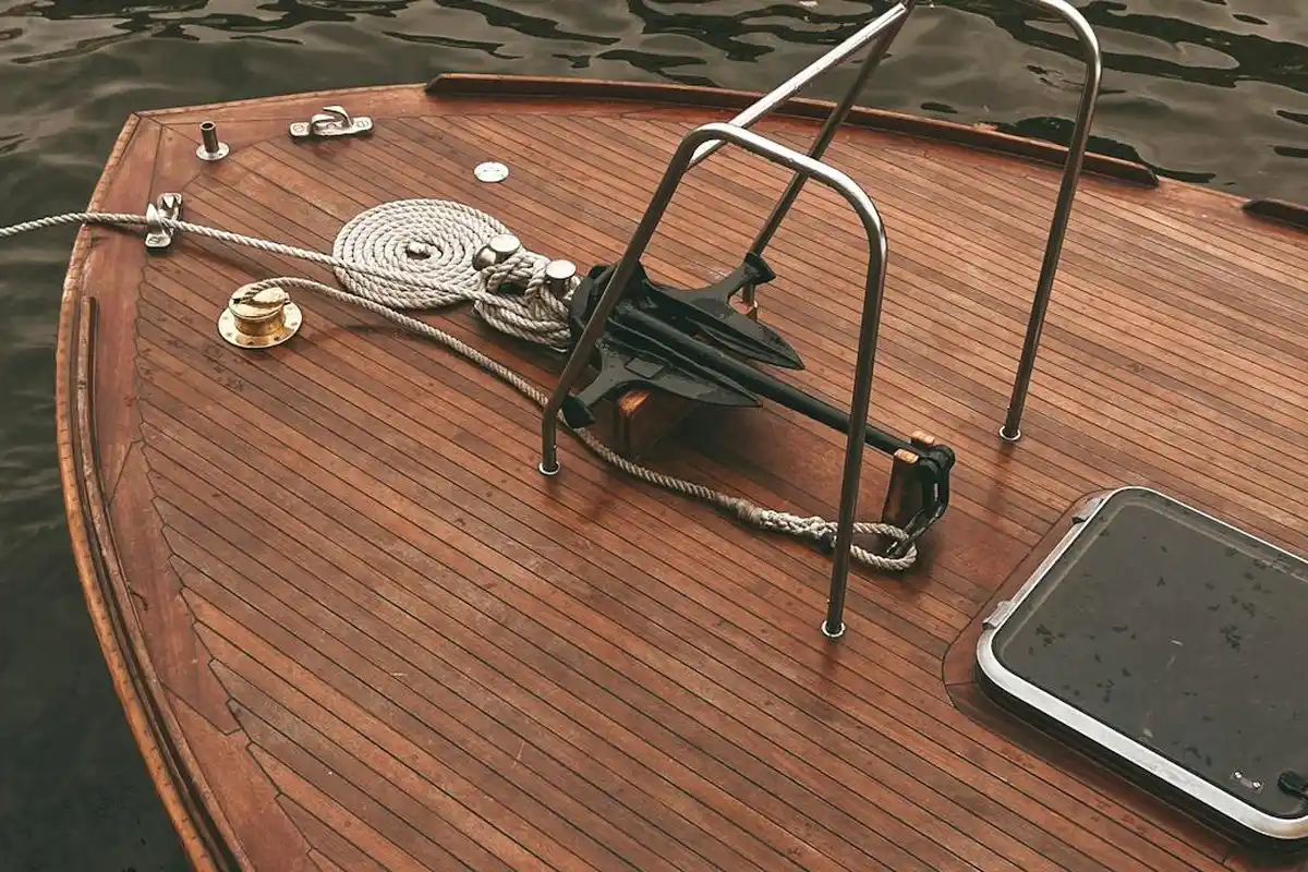 Close-up of a teak-toned wooden boat deck with rope, cleats, and a hatch.