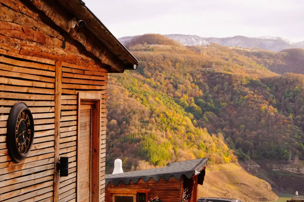 Wooden cabin exterior with a round clock on the wall, overlooking a valley of autumn-colored hills.