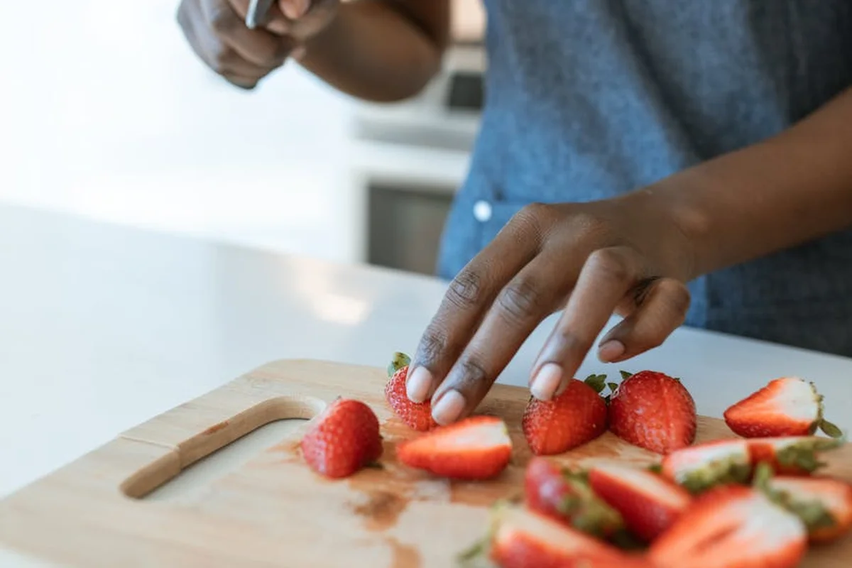 Close-up of hands slicing strawberries on a wooden cutting board in a bright kitchen.