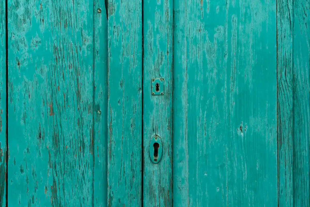 Teal-painted wooden door with vertical planks and a metal keyhole, symbolizing the head-to-head debates about wood hardness in Janka measurements.