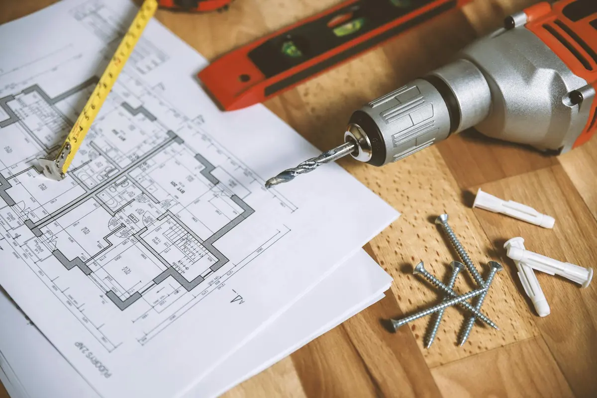Drill, blueprints, and tools on a wooden work surface, illustrating a technical spec review