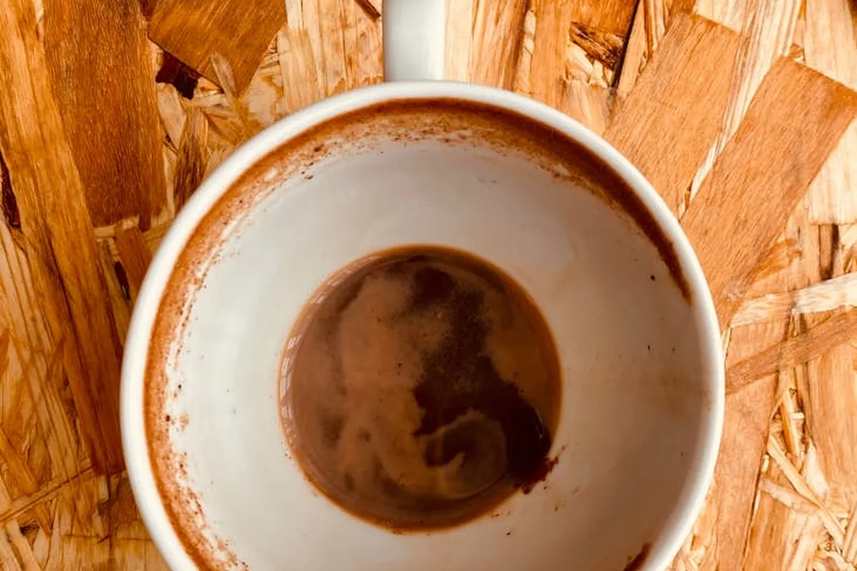 Top-down view of a coffee mug with stains on the interior placed on a rough OSB plywood surface, emphasizing wood texture.