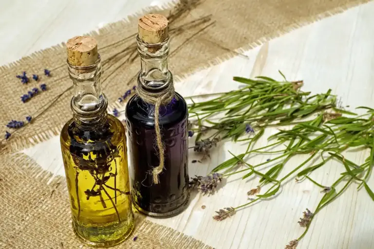 Two glass bottles with cork stoppers containing pale yellow and dark oil on a burlap surface, with lavender sprigs beside them.