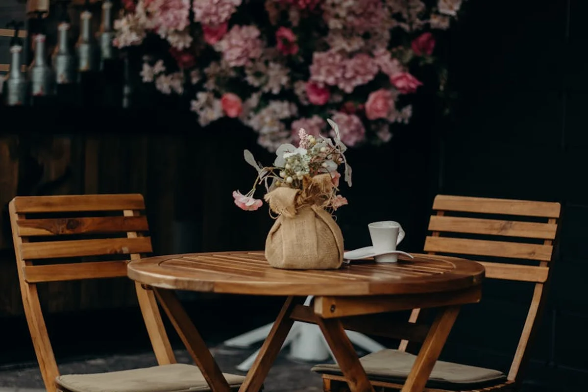 Round wooden outdoor table with two chairs, a burlap bouquet centerpiece, on a patio.