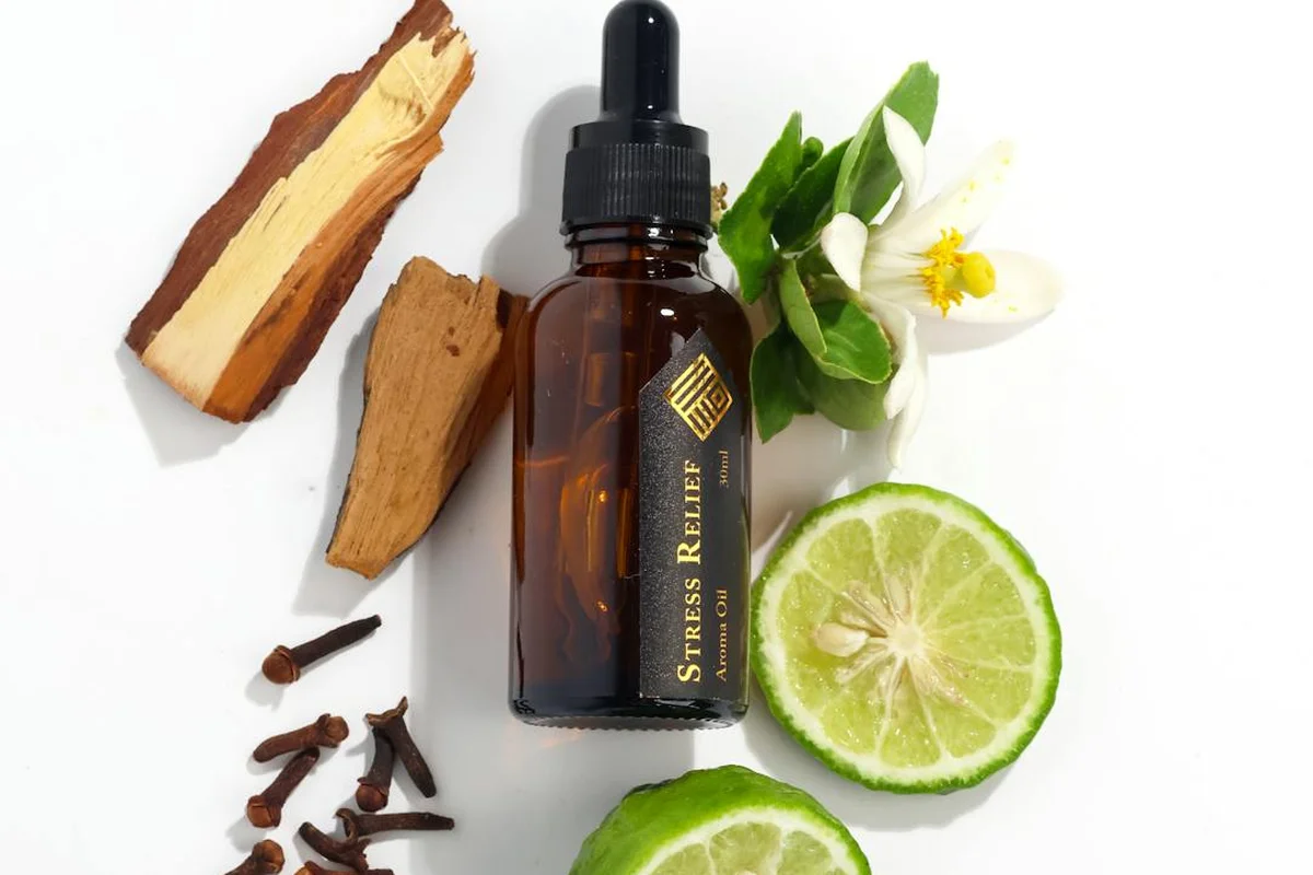 Amber glass dropper bottle surrounded by wood shavings, lime slices, and a white flower on a white background, suggesting natural drying oils such as tung oil and linseed oil.