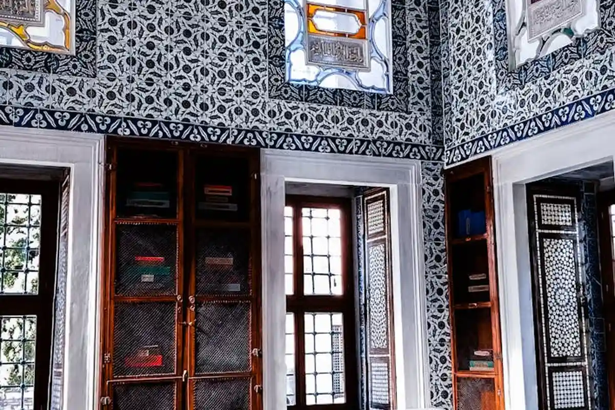 Ornate interior wall with blue and white patterned wallpaper and dark wood cabinets with glass doors.
