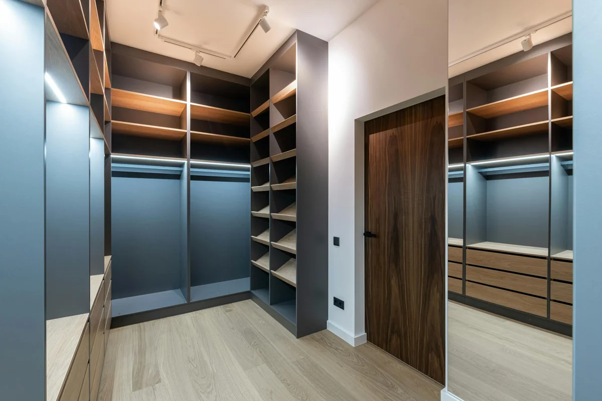 Interior walk-in closet with blue-gray built-in wardrobes, open shelves, and a wooden door.