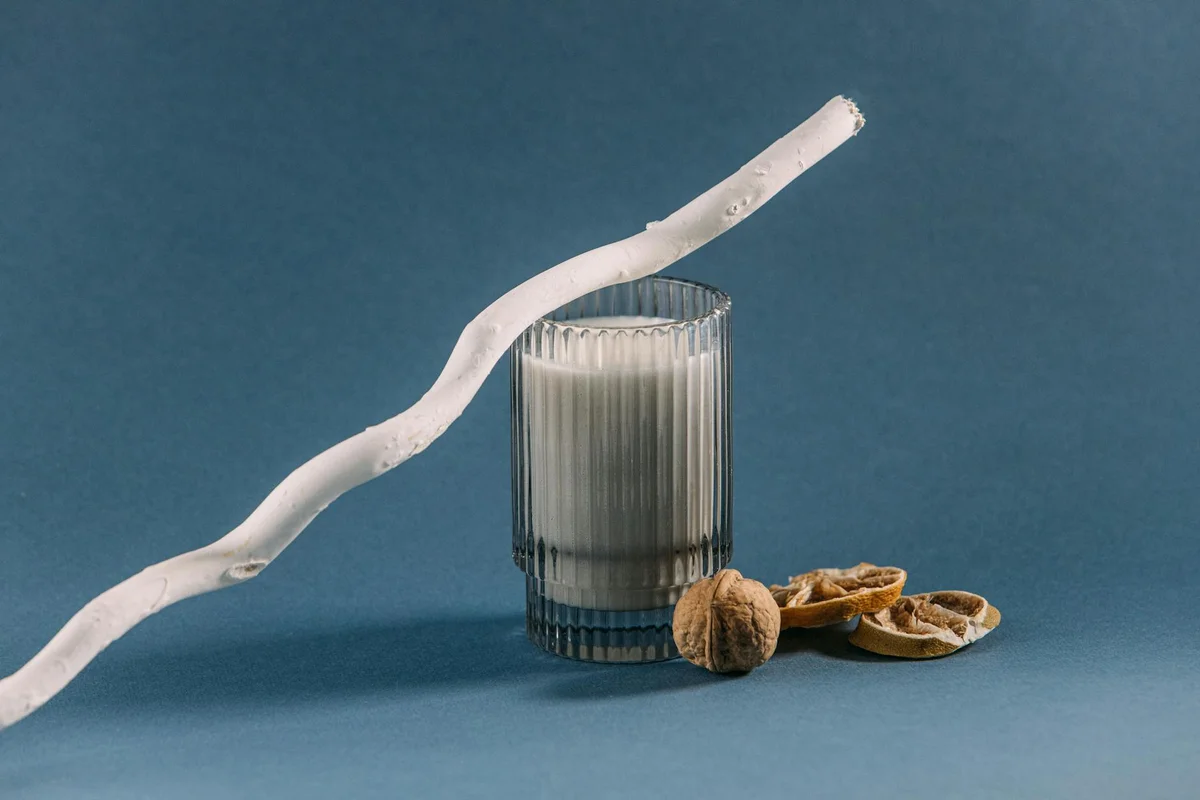 A glass with vertical ridges sits on a blue surface, with a white curved twig draped across it and walnut shells nearby.