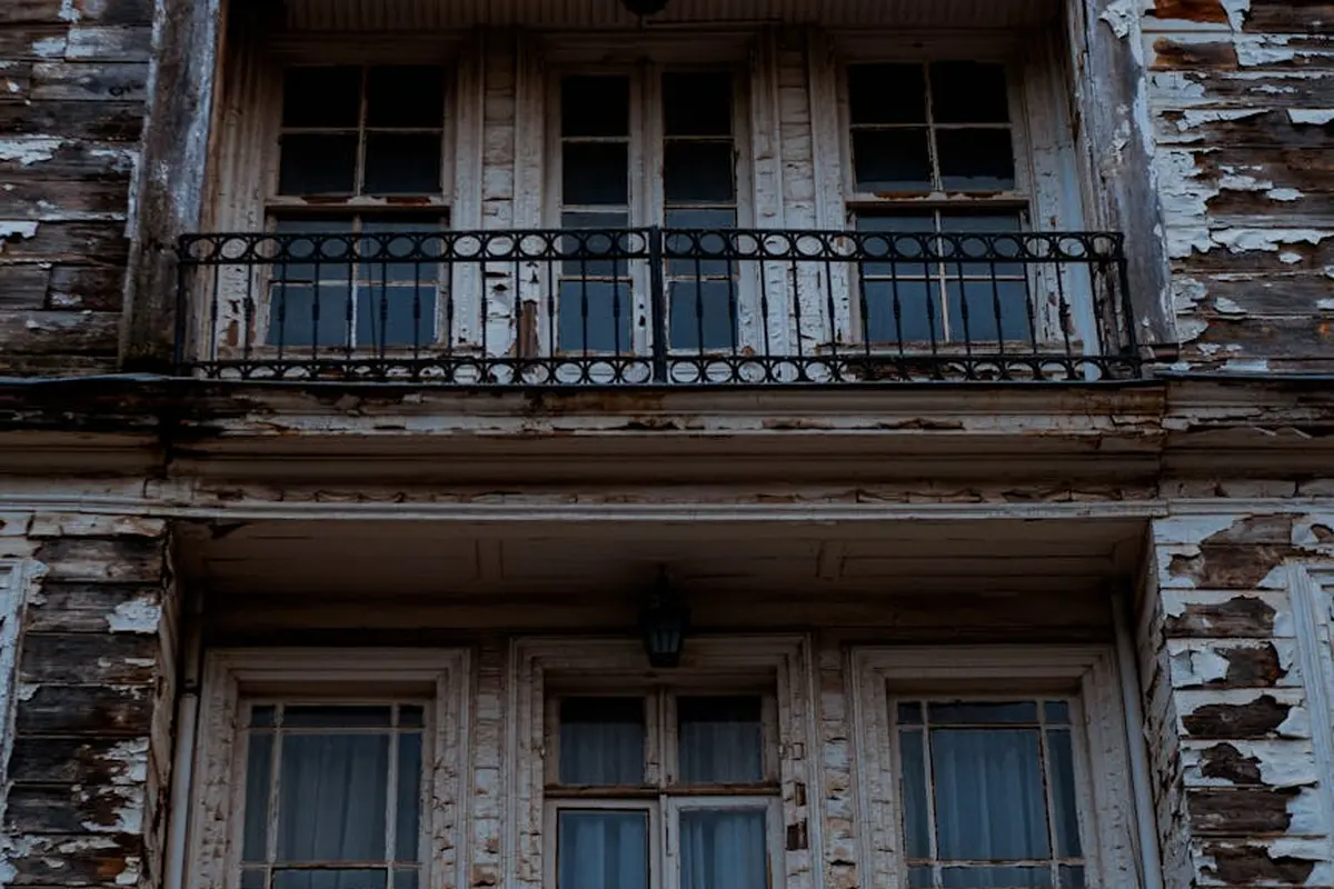 Weathered wooden exterior with peeling paint and a wrought-iron balcony railing