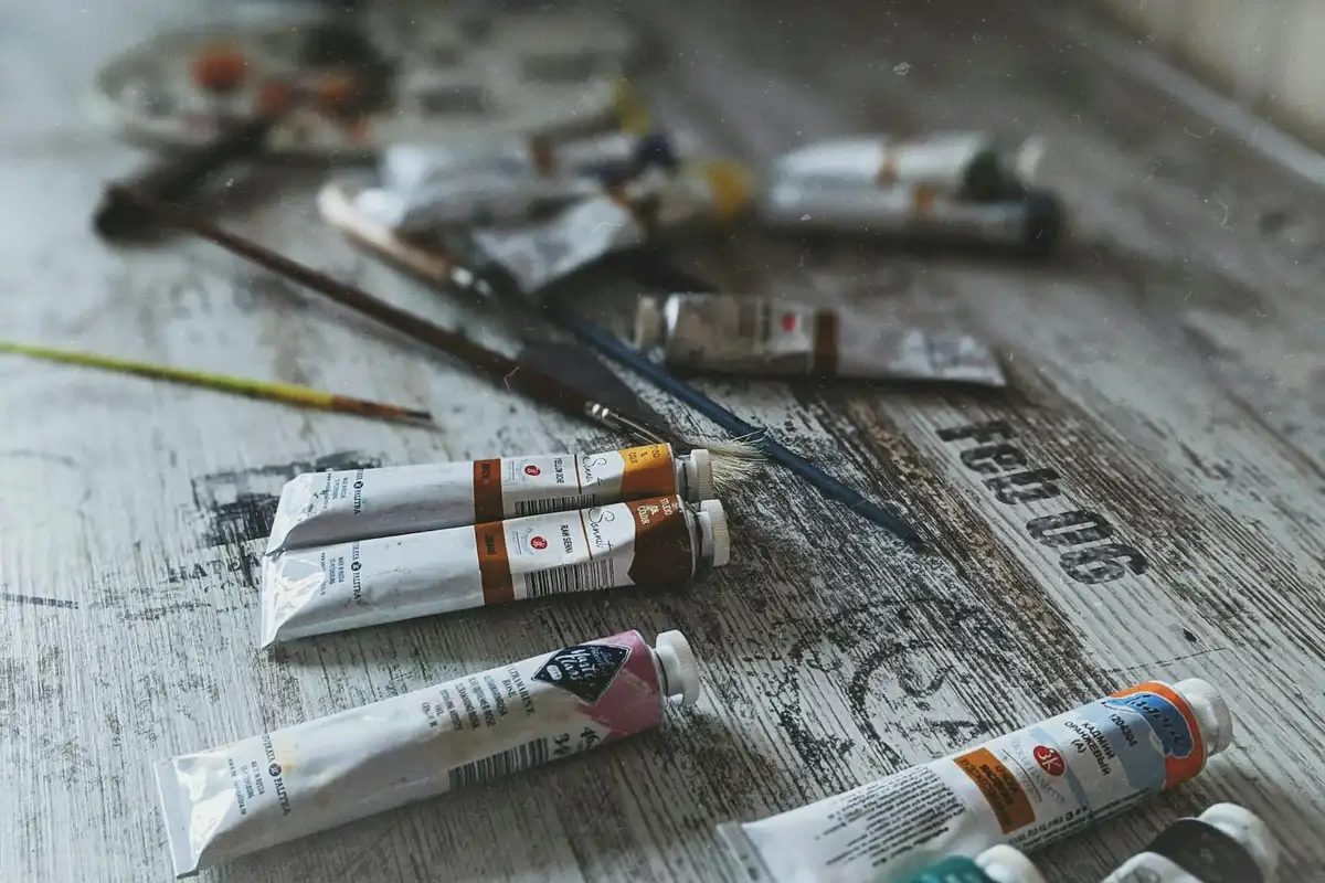 Assorted tubes of paint and brushes scattered on a weathered wooden work surface