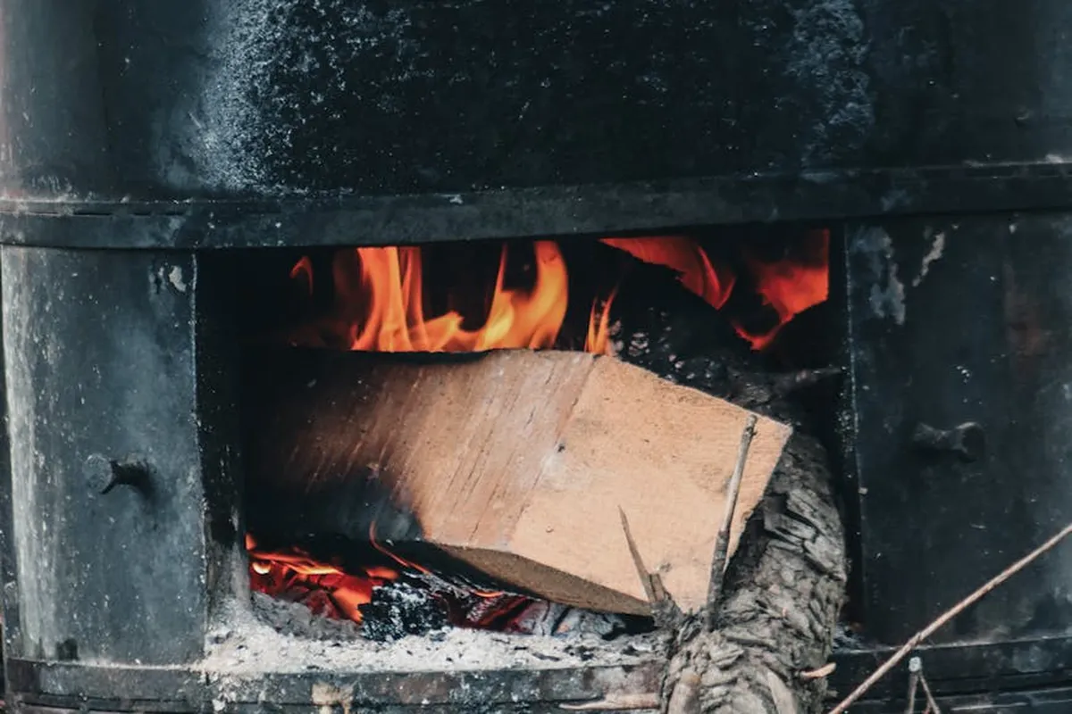 Inside a metal wood-burning barrel stove, a log is burning with orange flames and glowing embers.