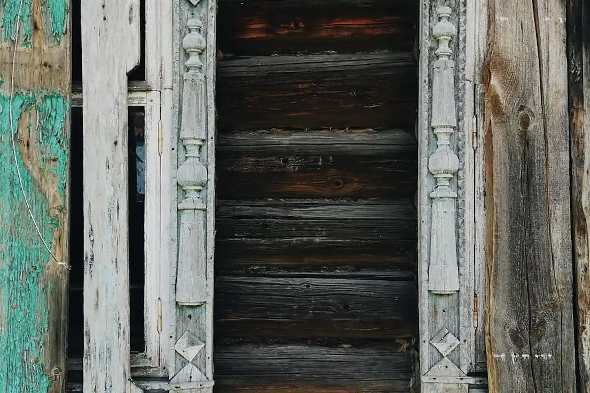 Weathered wooden doorway with peeling paint and ornate trim showing water damage