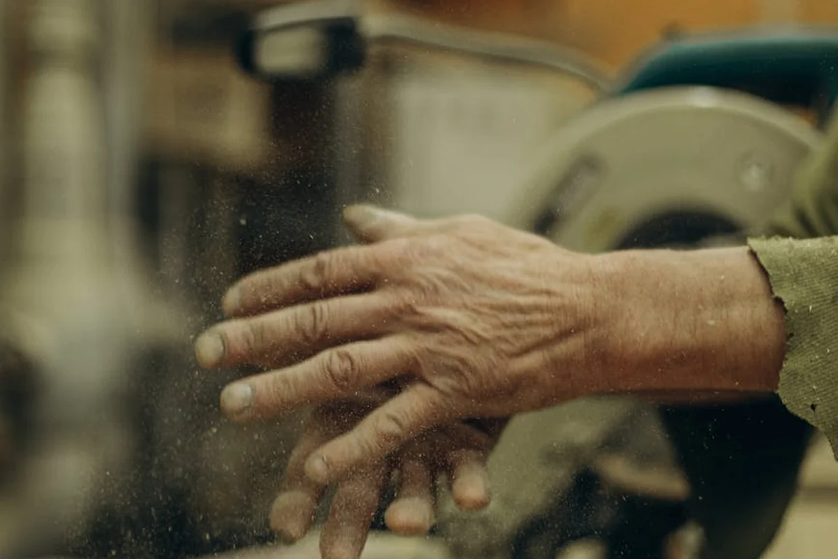 Close-up of a woodworker's hand in a workshop with fine wood dust particles in the air